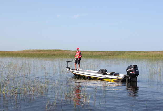 man working trolling motor on front of bass boat in lake